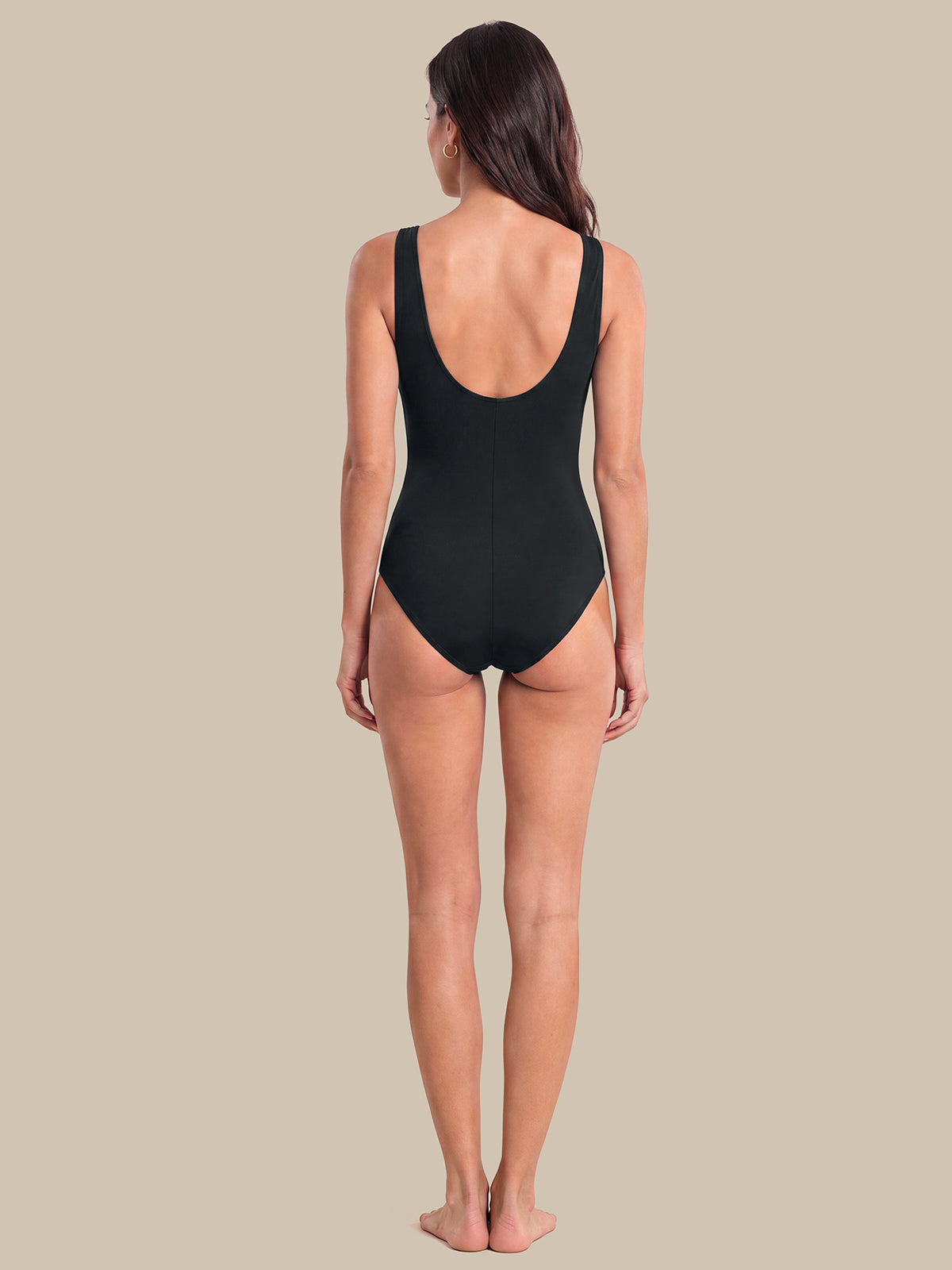 A woman viewed from the back wearing a black one-piece swimsuit, standing against a solid beige background.