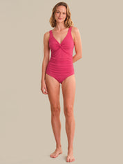 Woman wearing a pink one-piece swimsuit on a beige background