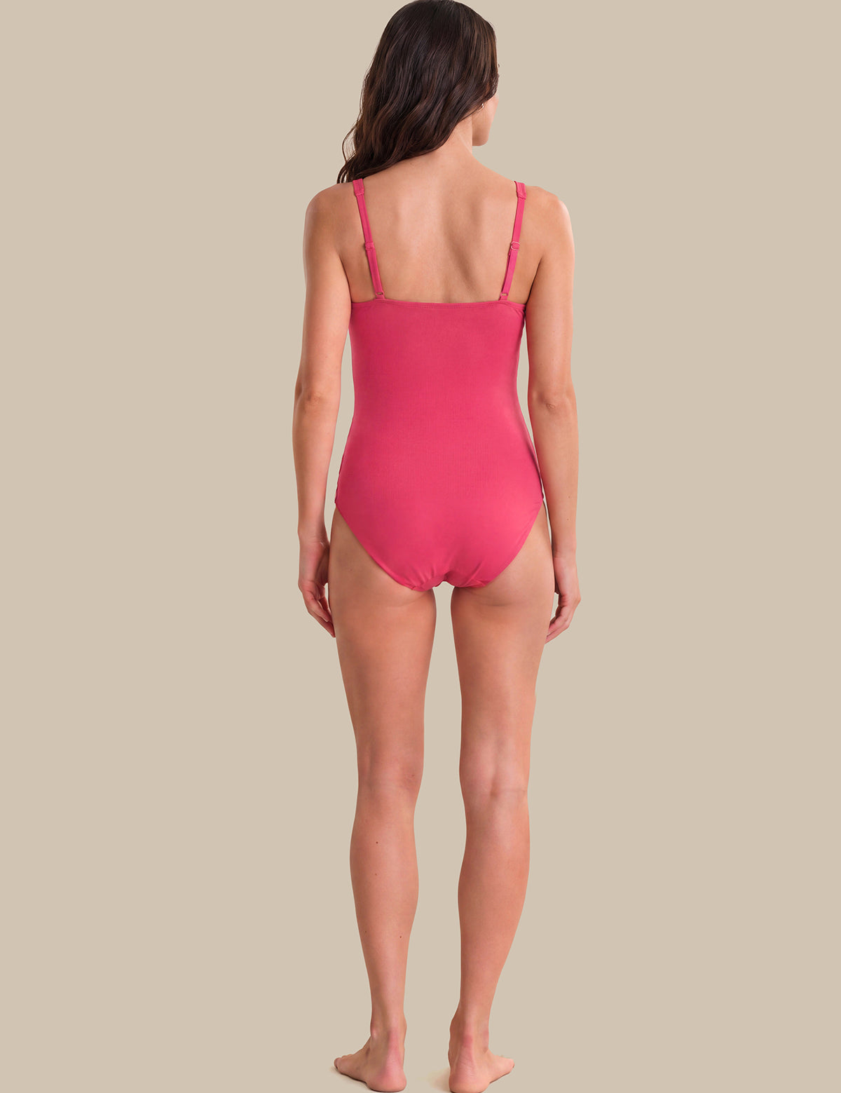 A woman viewed from the back wearing a bright pink one-piece swimsuit, standing against a solid beige background.