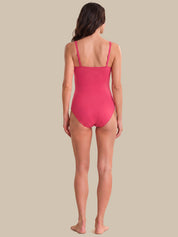 A woman viewed from the back wearing a bright pink one-piece swimsuit, standing against a solid beige background.