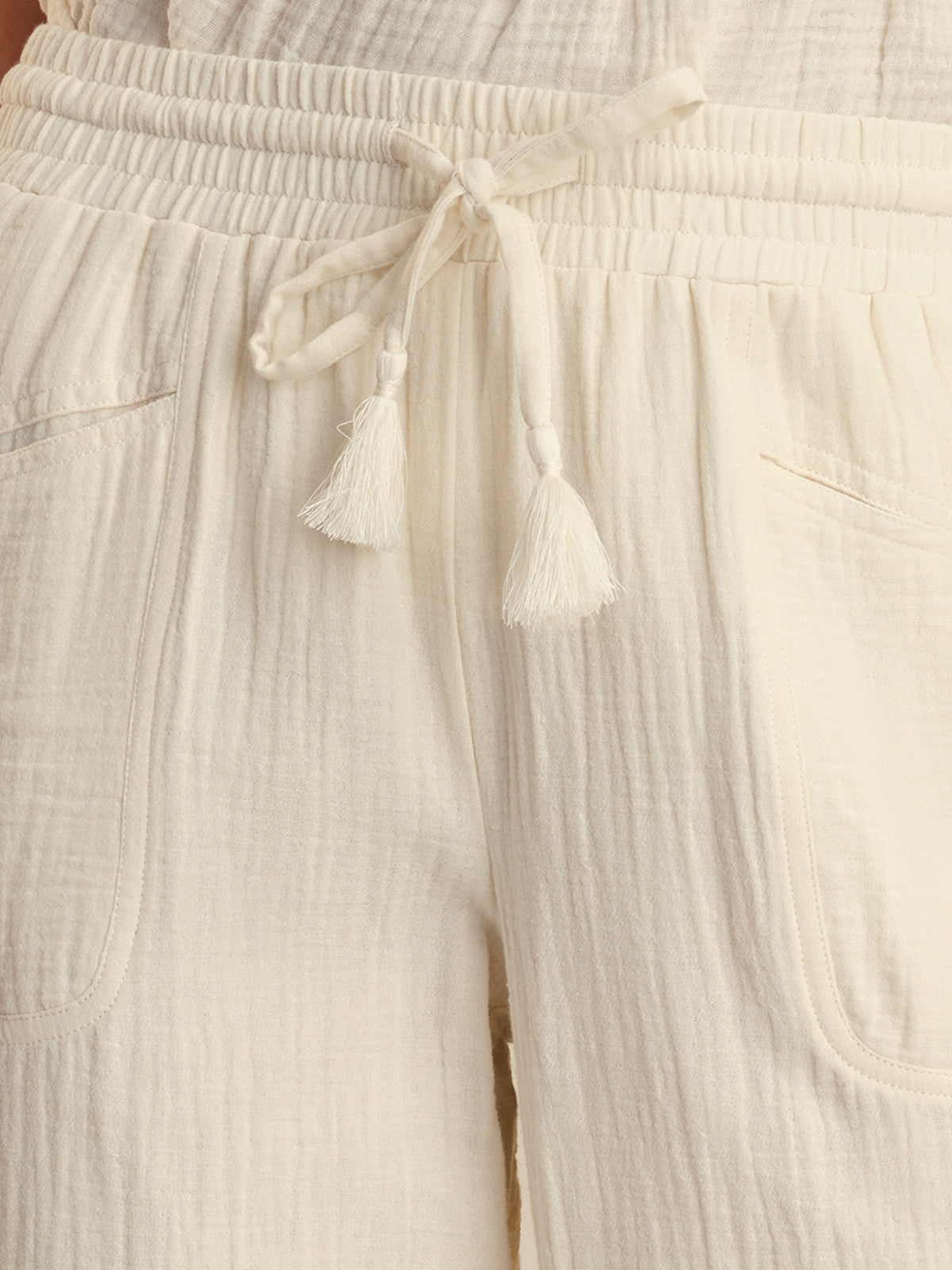 Close-up of beige pants with a drawstring and tassels.