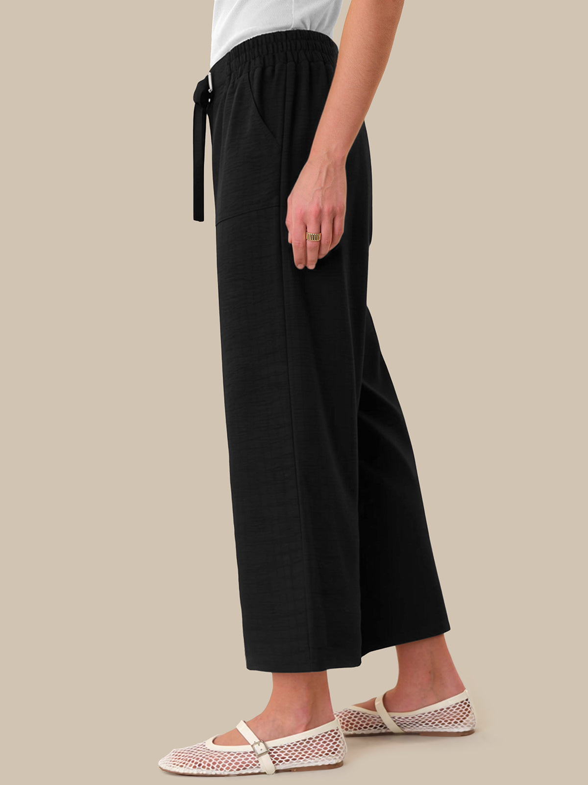 Person wearing black wide-leg pants on a beige background