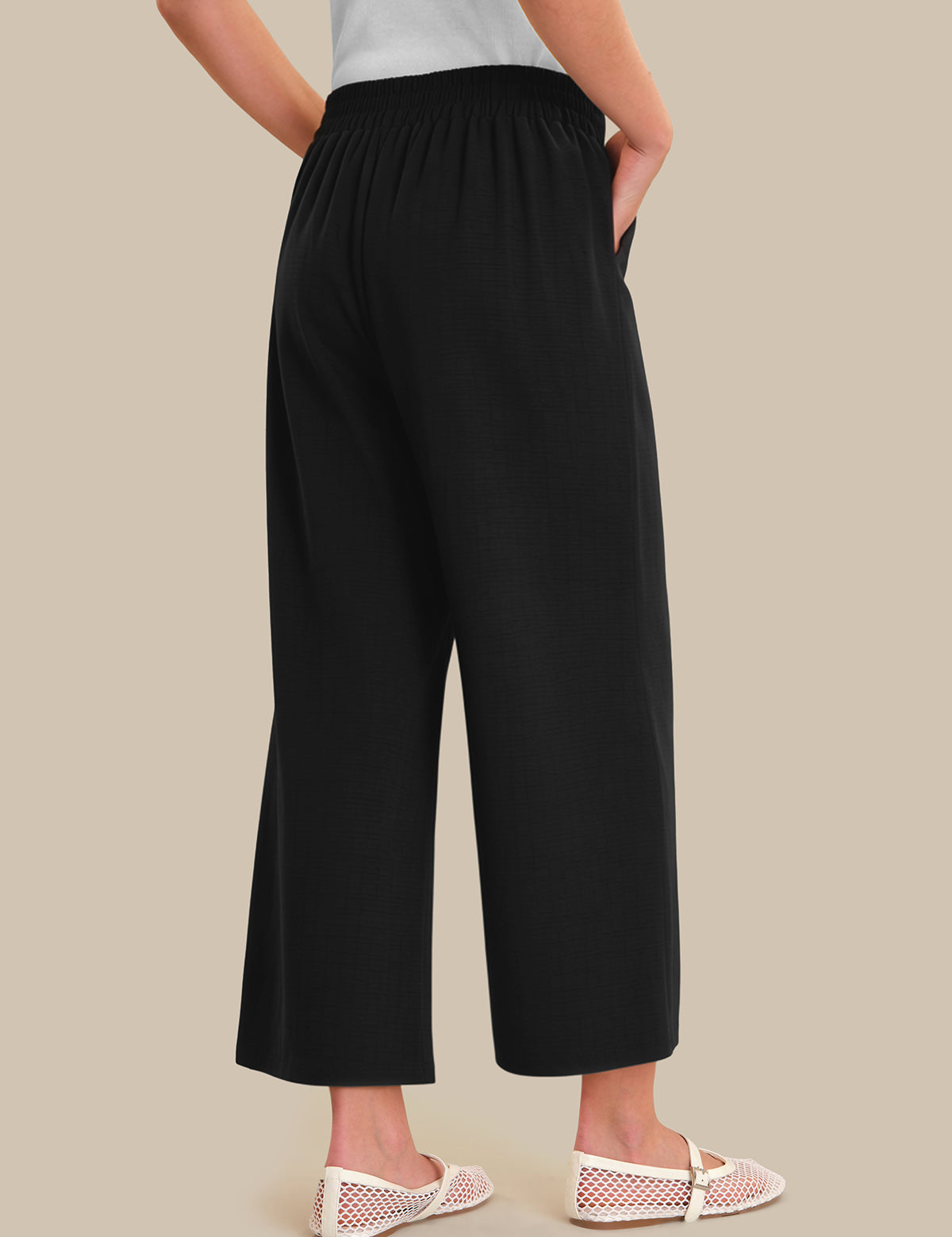 Person wearing black wide-leg pants on a beige background