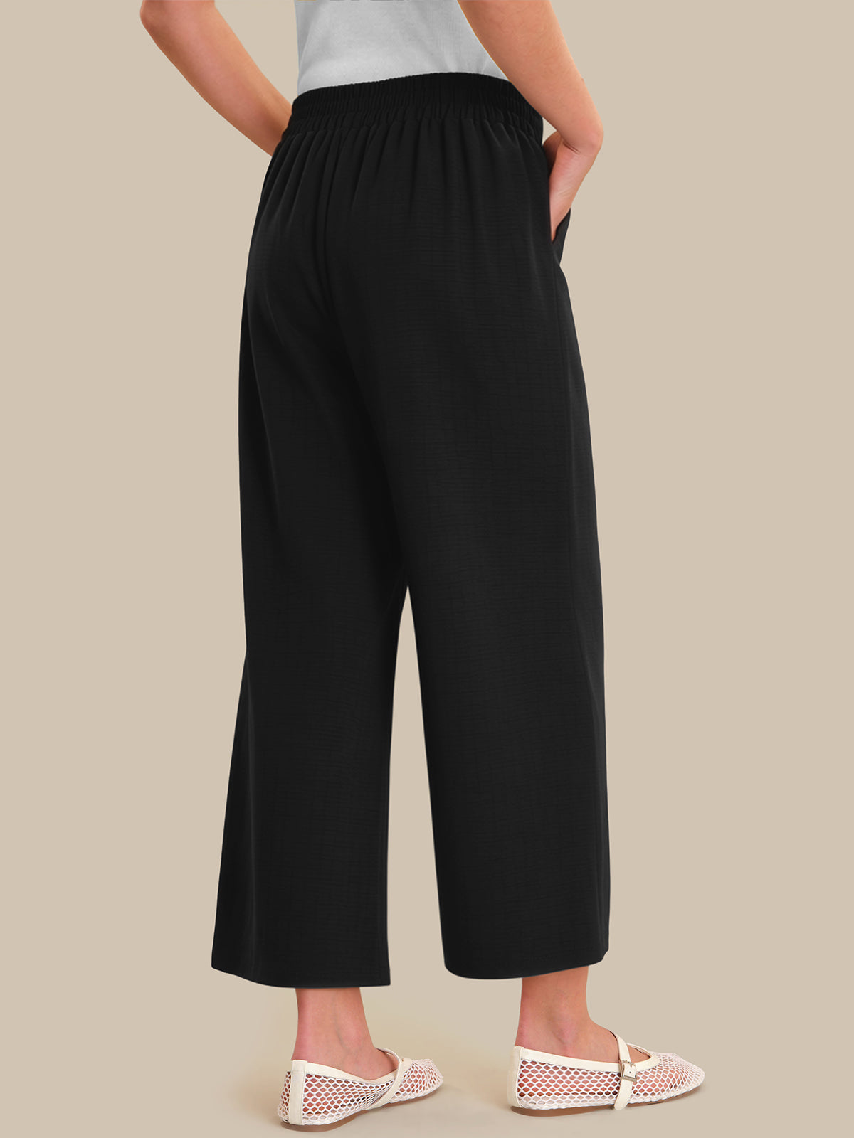 Person wearing black wide-leg pants on a beige background