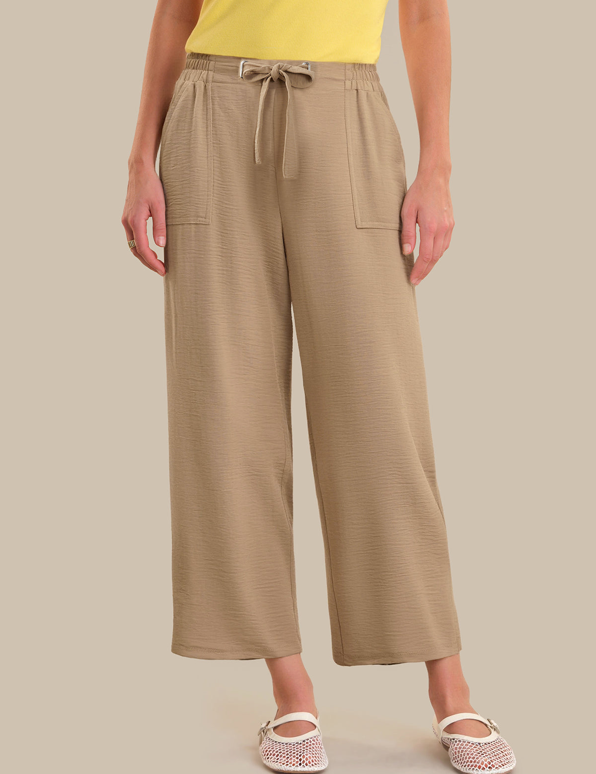 Person wearing beige wide-leg pants with a yellow top on a neutral background
