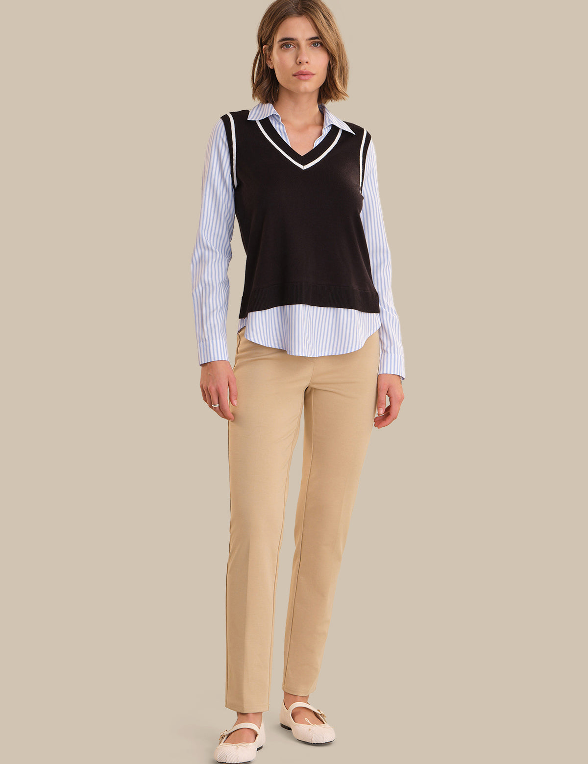 Woman wearing a black sweater over a striped shirt with beige pants on a beige background