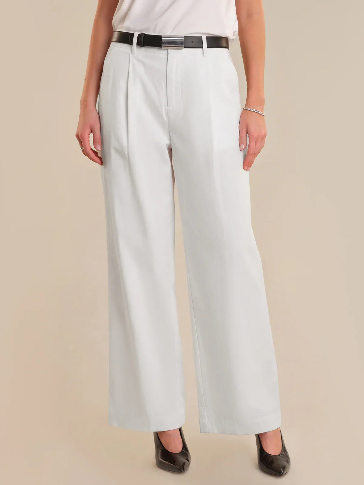 Person wearing white wide-leg pants with a black belt on a beige background