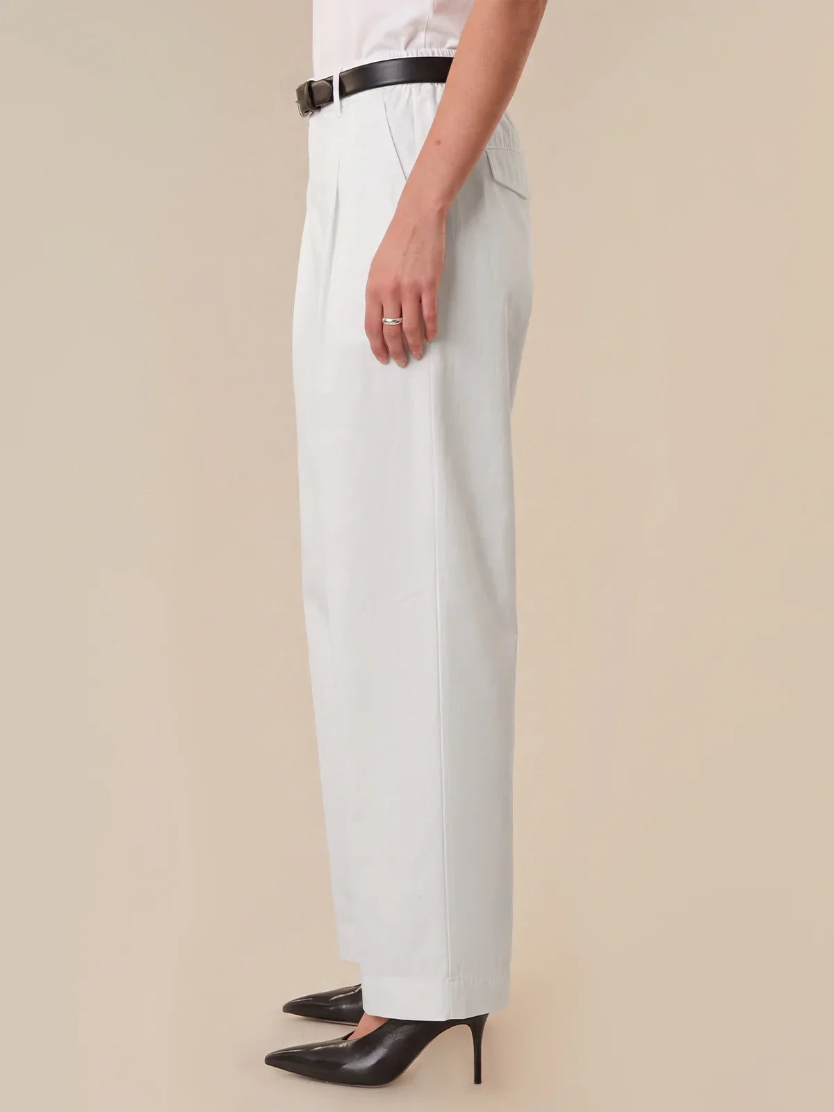 Person wearing light blue pants with a black belt on a beige background