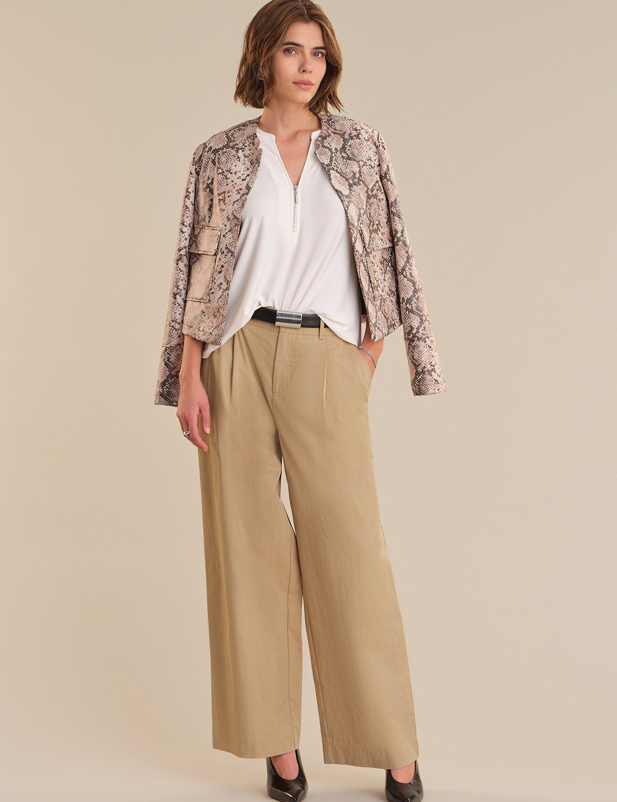 Woman wearing a patterned jacket, white shirt, and beige pants on a beige background