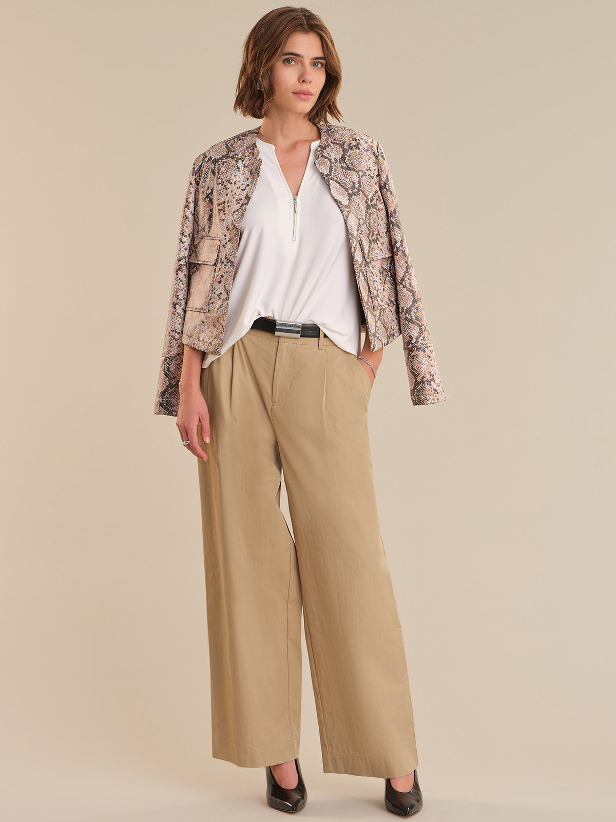 Woman wearing a patterned jacket, white shirt, and beige pants on a beige background