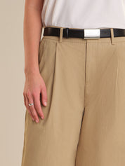 Person wearing beige pants with a black belt and silver buckle on a beige background