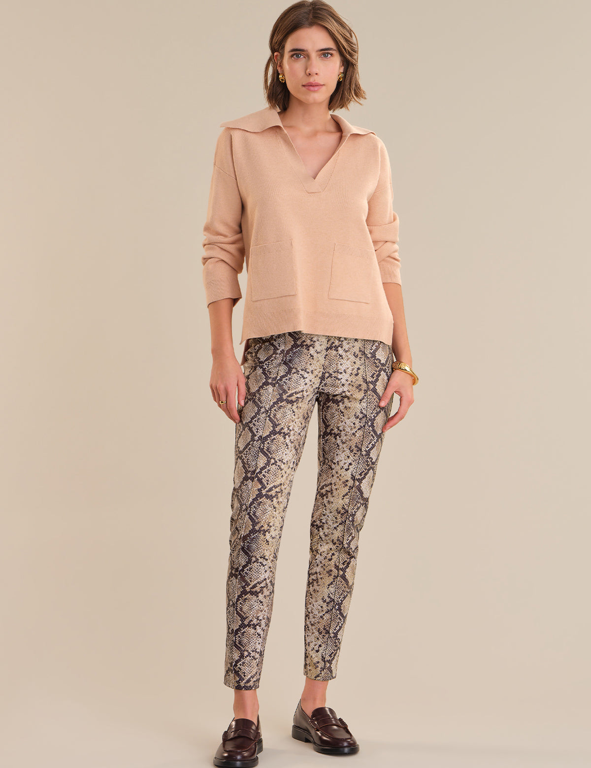 Woman wearing a beige jacket and snake print pants on a beige background