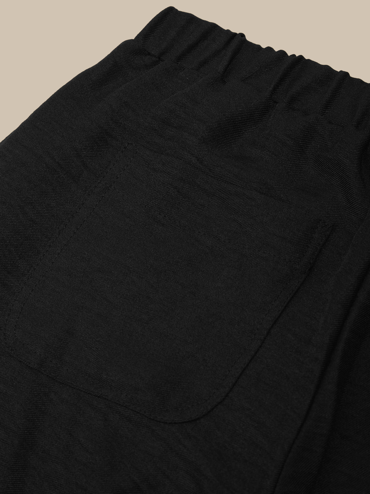 Close-up of black pants with a pocket on a beige background