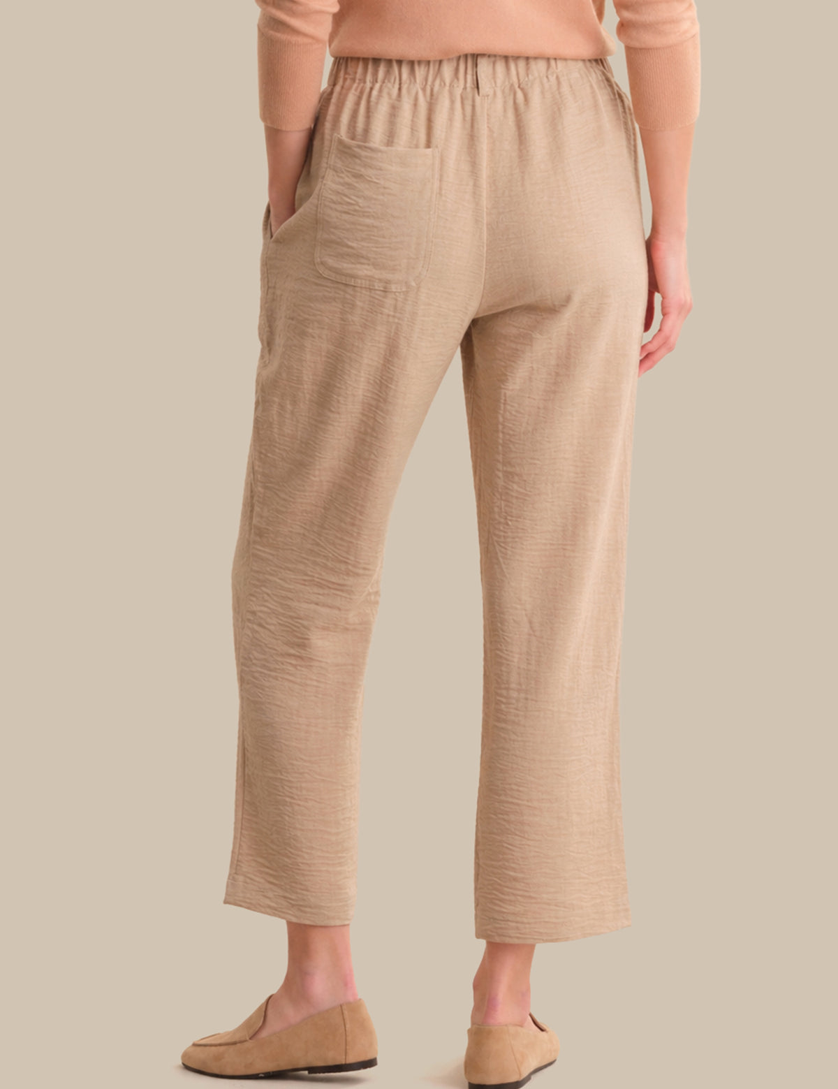 Person wearing beige pants and a matching top on a plain background