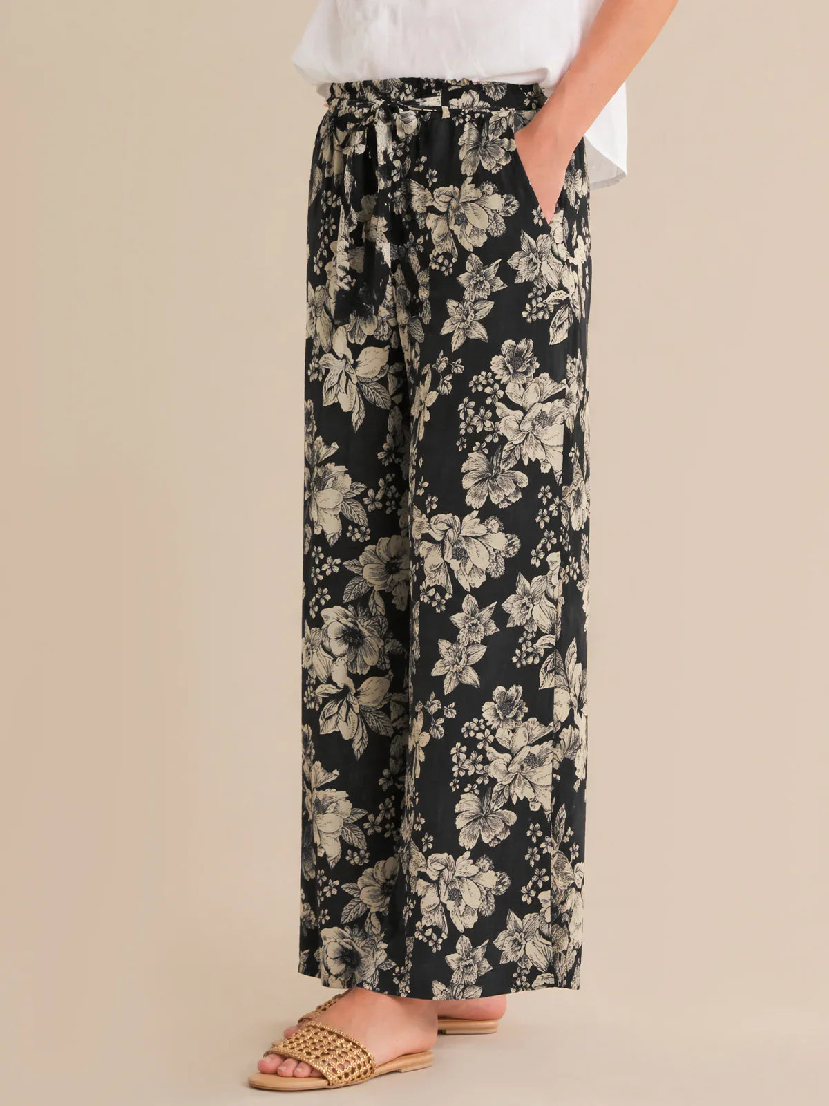 Black floral pants worn by a person on a beige background