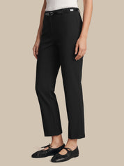 A model wearing black cropped trousers with a black belt, paired with black flat shoes, shown from the waist down against a solid beige background.
