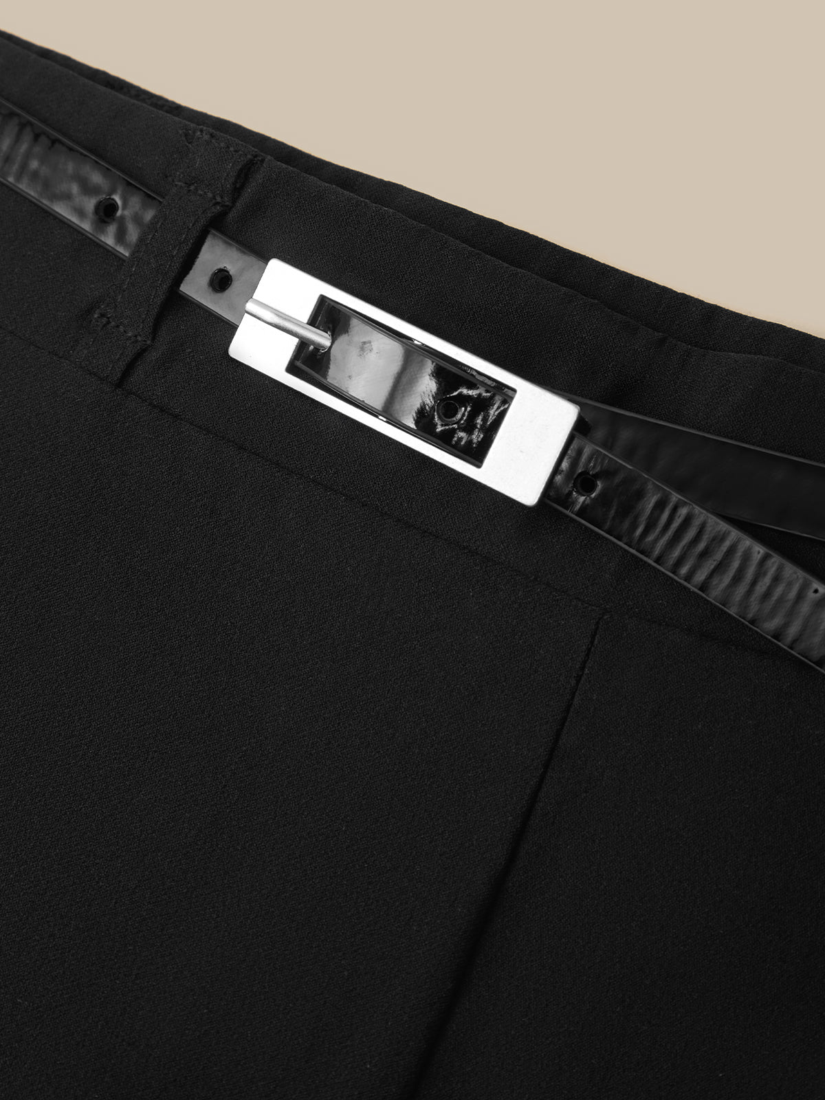 Close-up of a black garment, likely a skirt or pants, featuring a wide silver-toned rectangular metal belt buckle with a black textured strap.