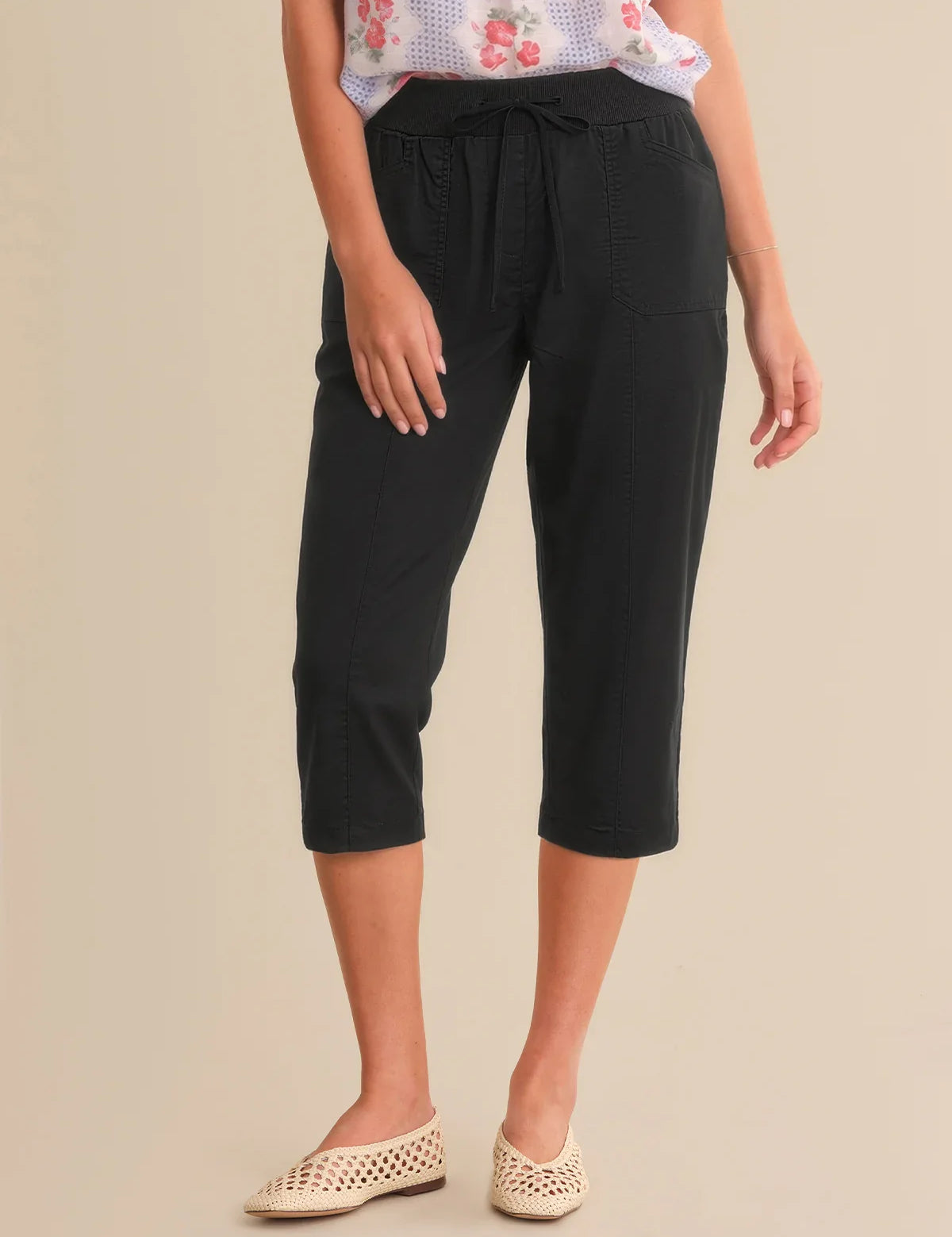 Person wearing black capri pants on a beige background