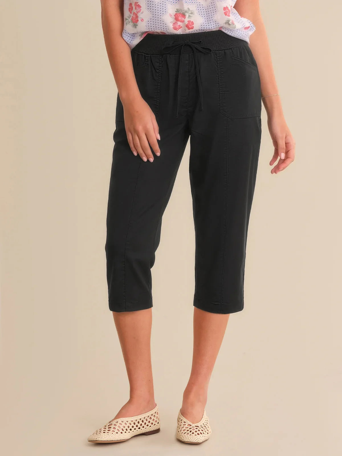 Person wearing black capri pants on a beige background