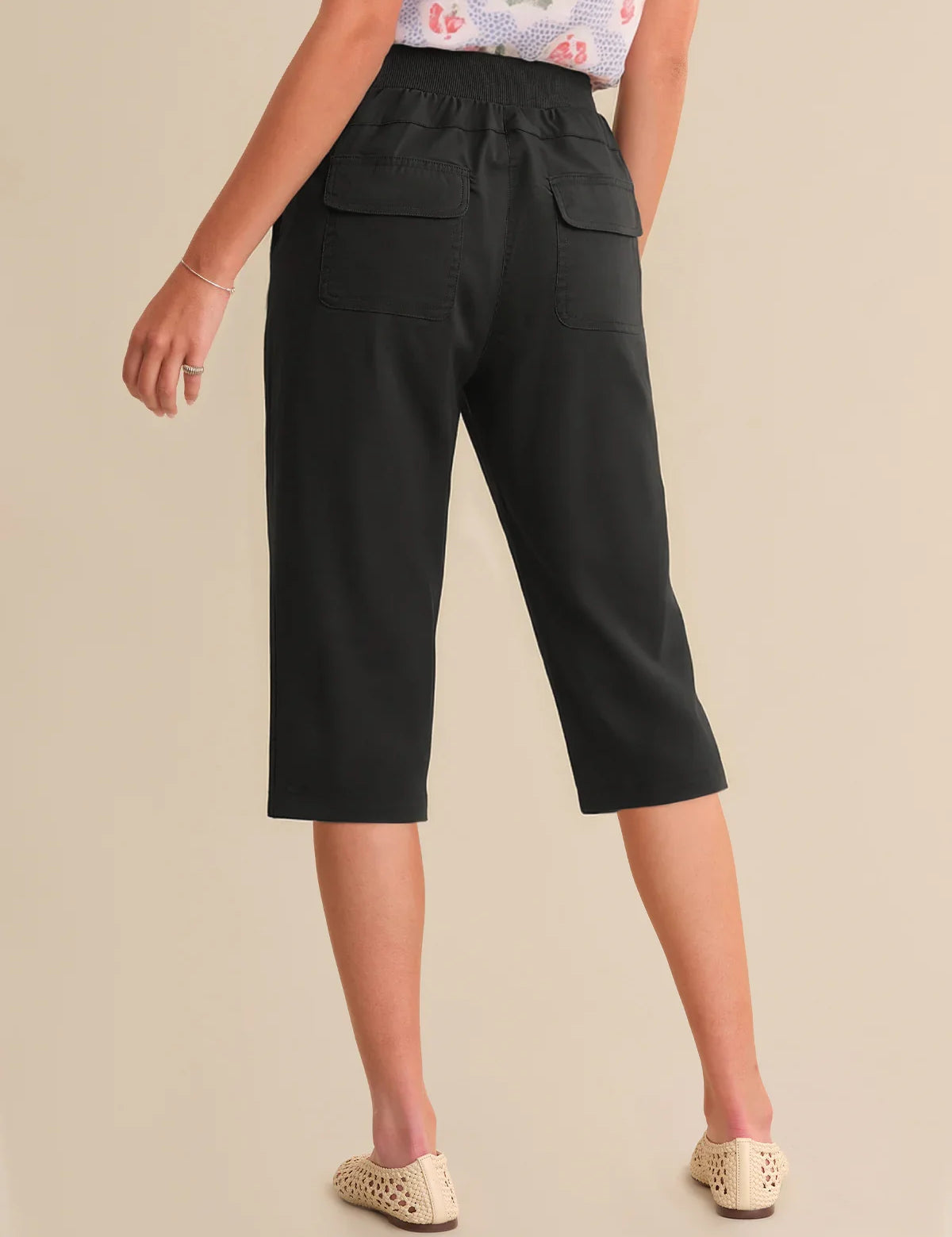 Person wearing black capri pants on a beige background