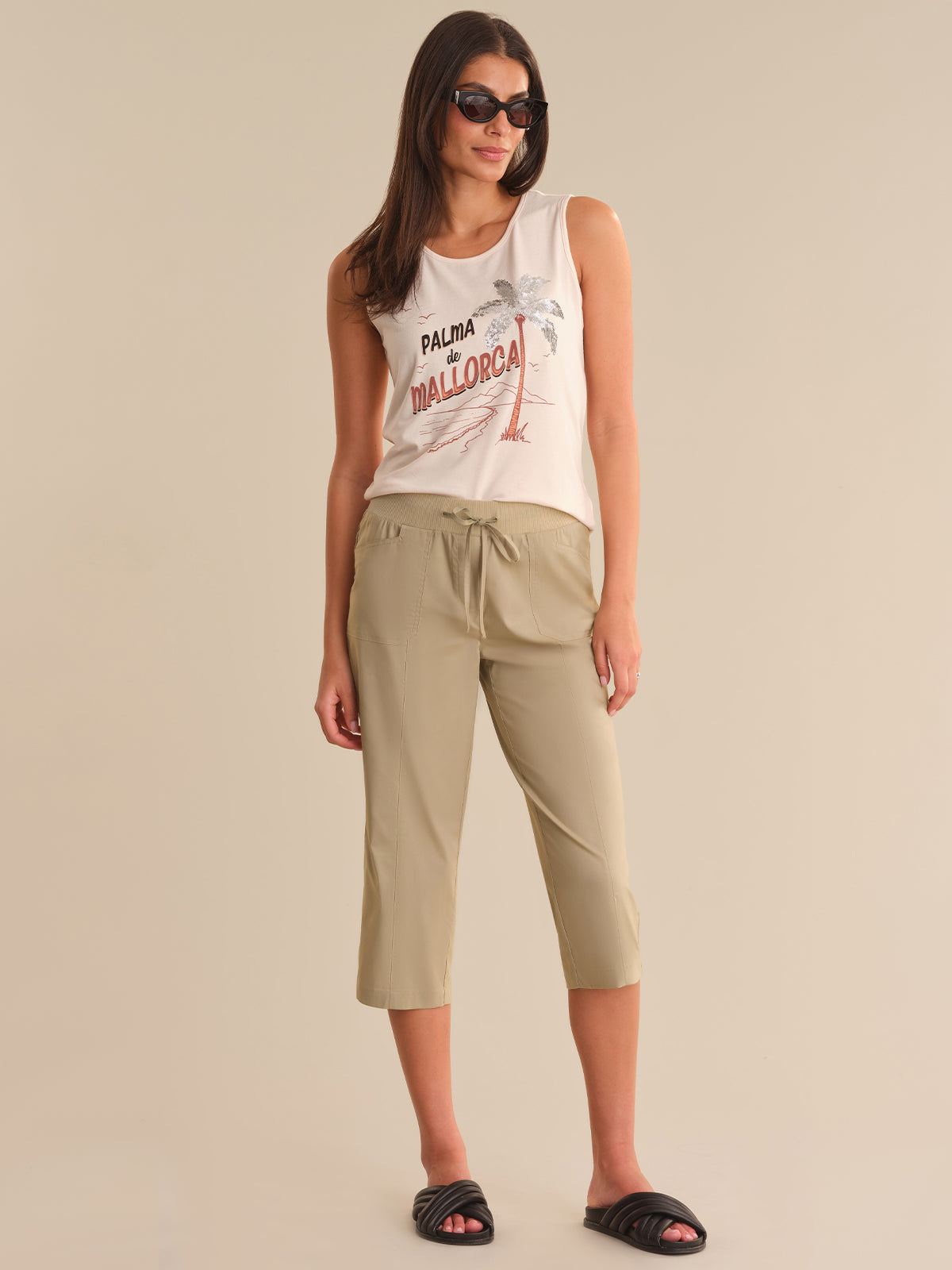 Woman wearing a sleeveless top and beige capri pants on a beige background