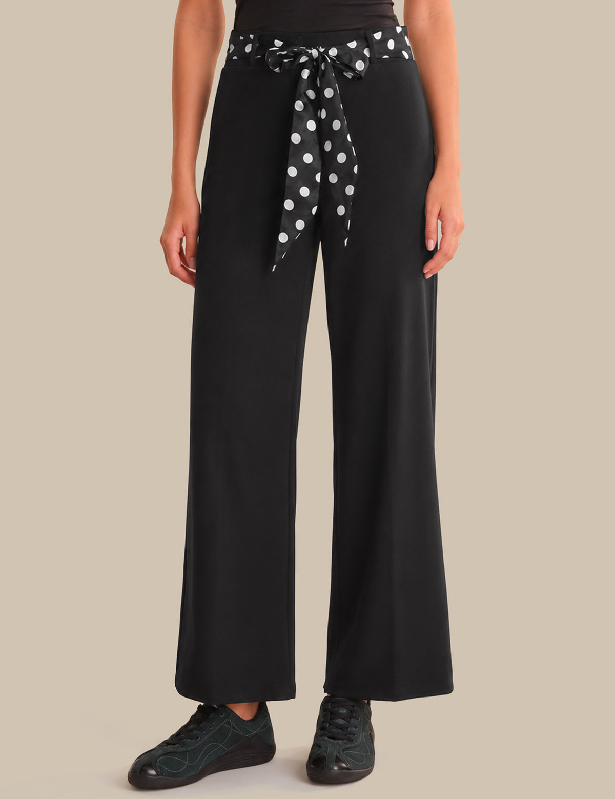 Person wearing black wide-leg pants with a polka dot belt on a beige background