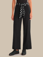 Person wearing black wide-leg pants with a polka dot belt on a beige background