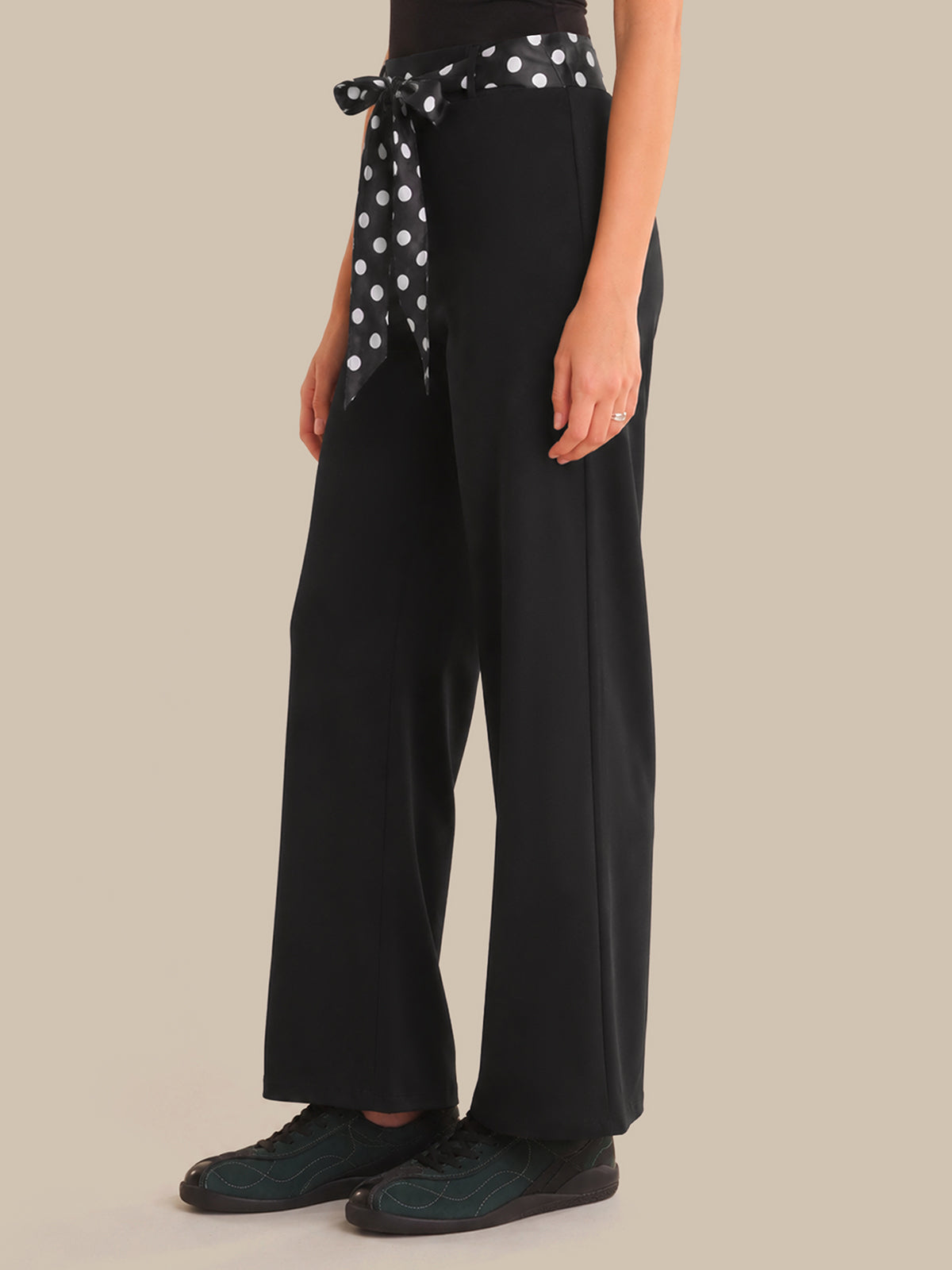 Person wearing black wide-leg pants with a polka dot scarf tied around the waist on a beige background