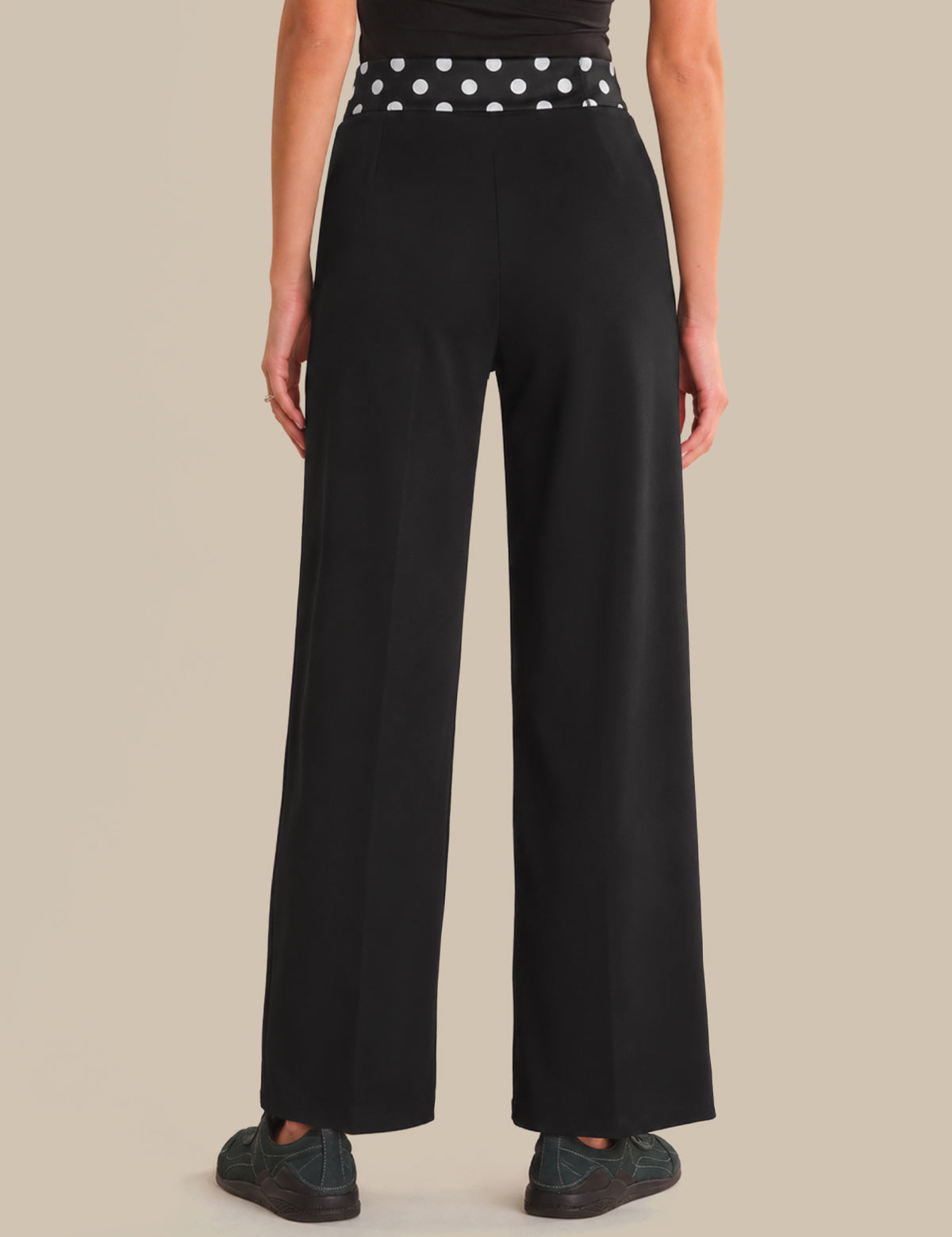 Person wearing black wide-leg pants with a polka dot belt on a beige background