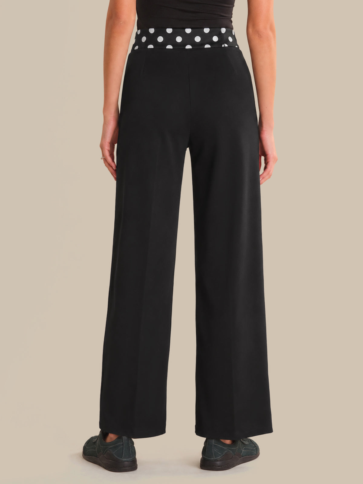 Person wearing black wide-leg pants with a polka dot belt on a beige background