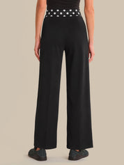 Person wearing black wide-leg pants with a polka dot belt on a beige background
