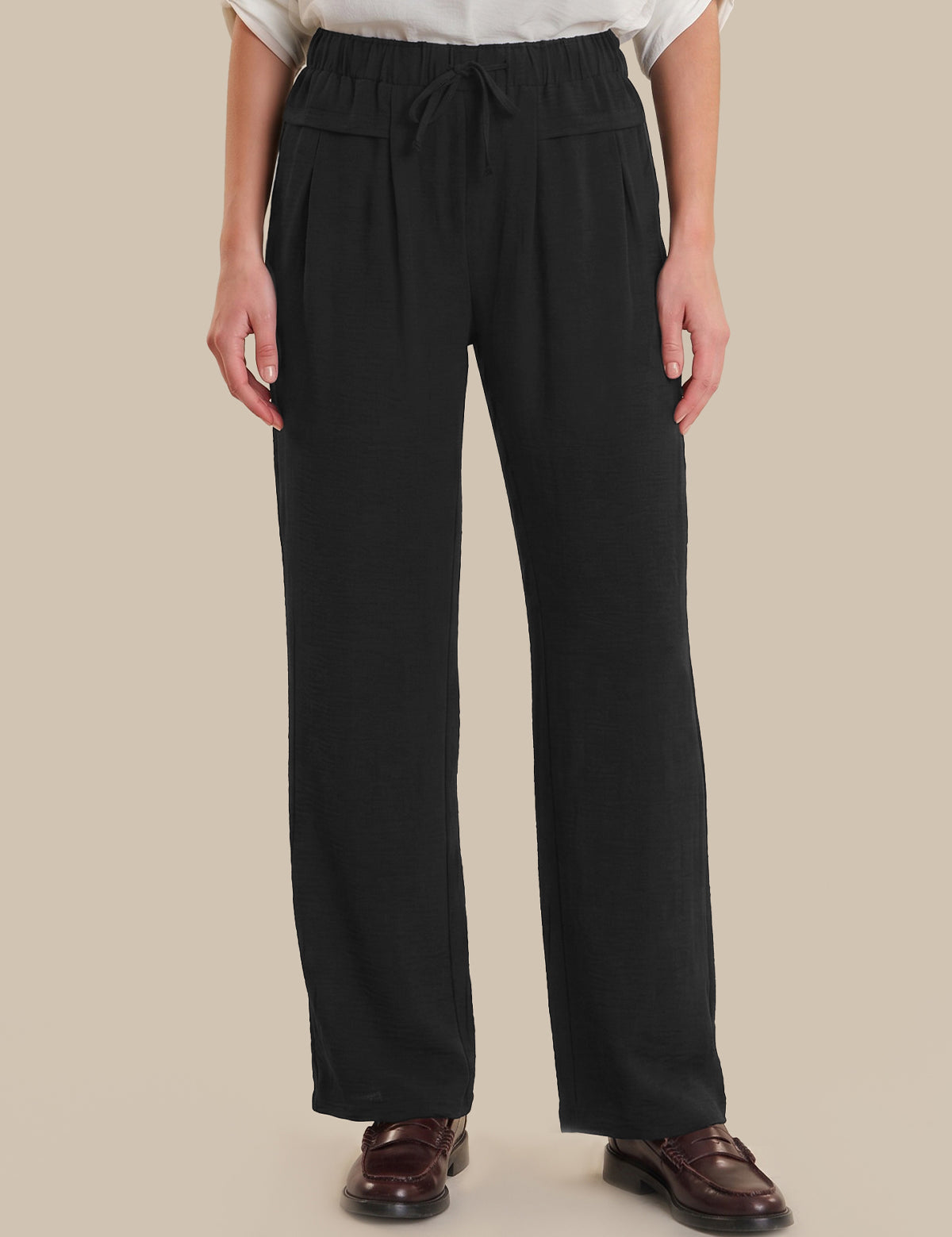 Person wearing black wide-leg pants on a beige background