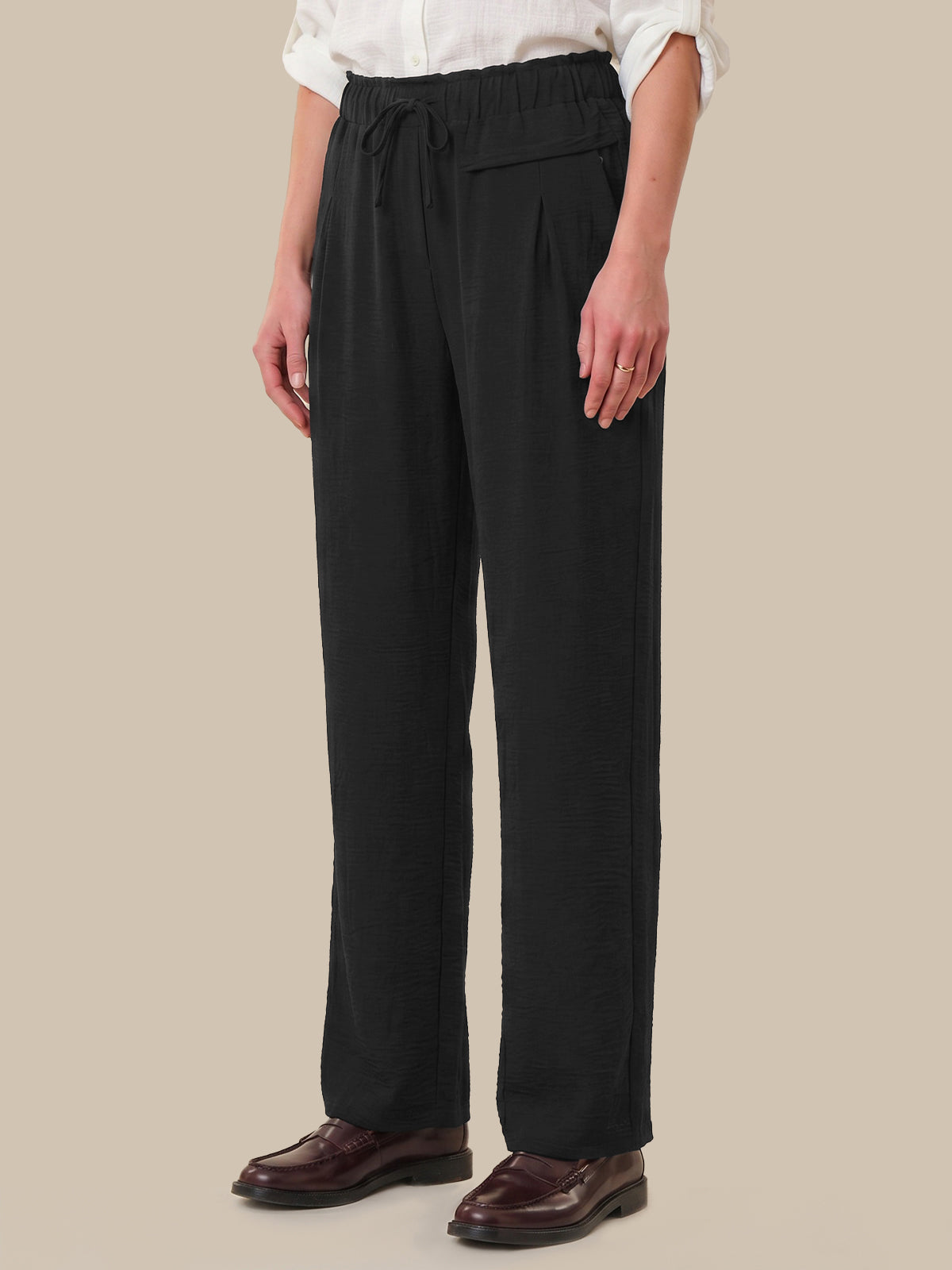 Person wearing black pants and a white shirt on a beige background