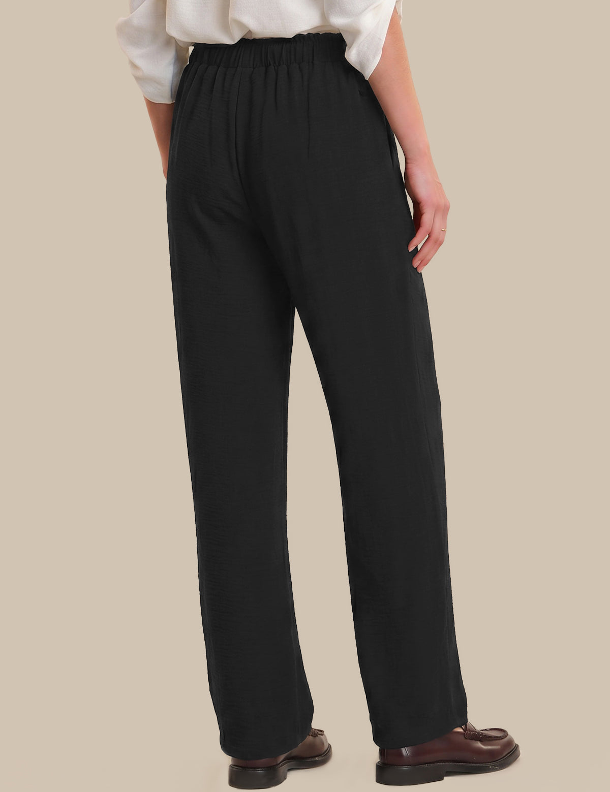Person wearing black pants and a white shirt on a beige background