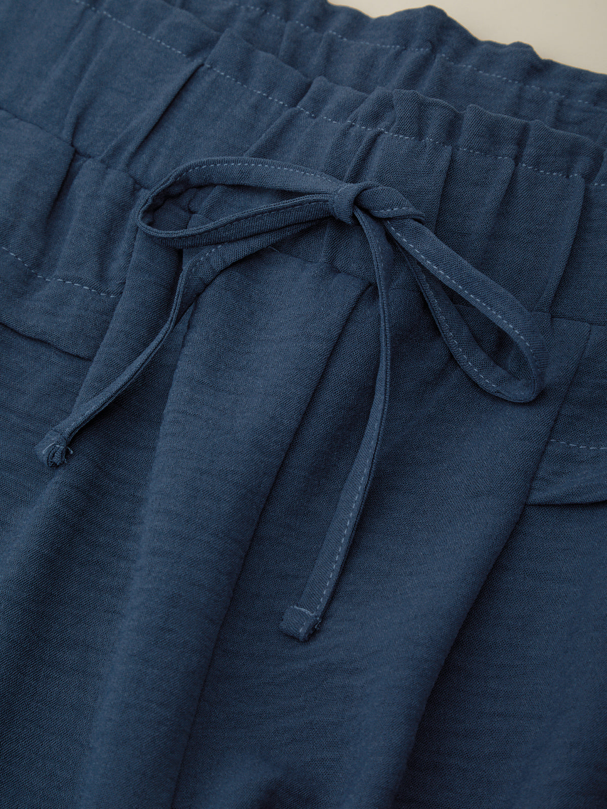 Close-up of blue pants with a tie waist on a neutral background
