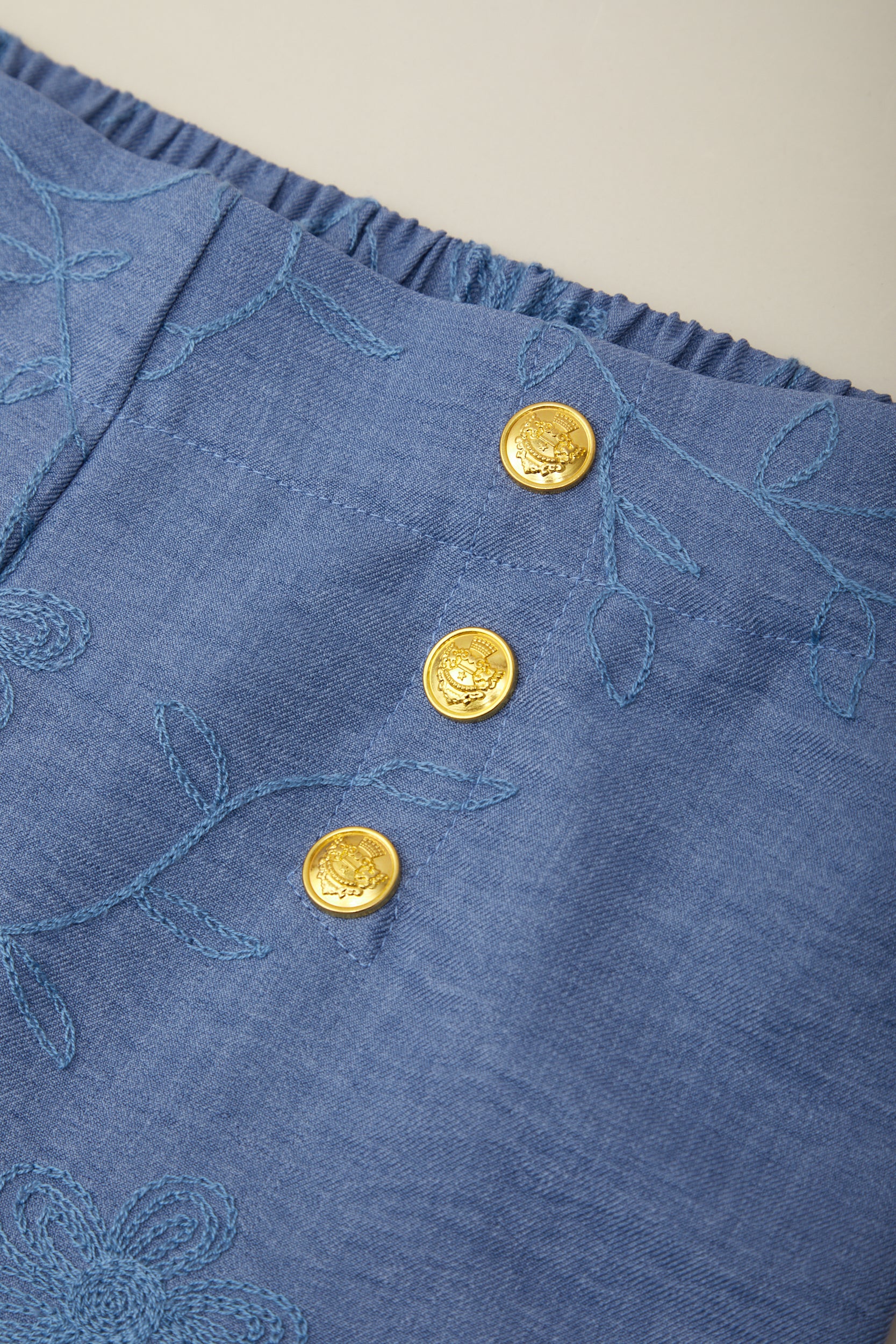 Blue fabric with gold buttons and floral embroidery on a beige background