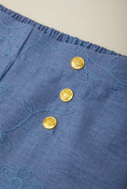 Blue fabric with gold buttons and floral embroidery on a beige background