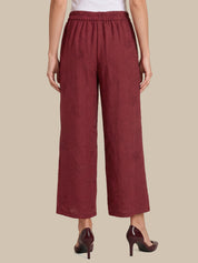 A model is shown from the back wearing a pair of wide-leg cropped pants in a textured burgundy fabric, paired with dark burgundy high heels against a solid beige background.