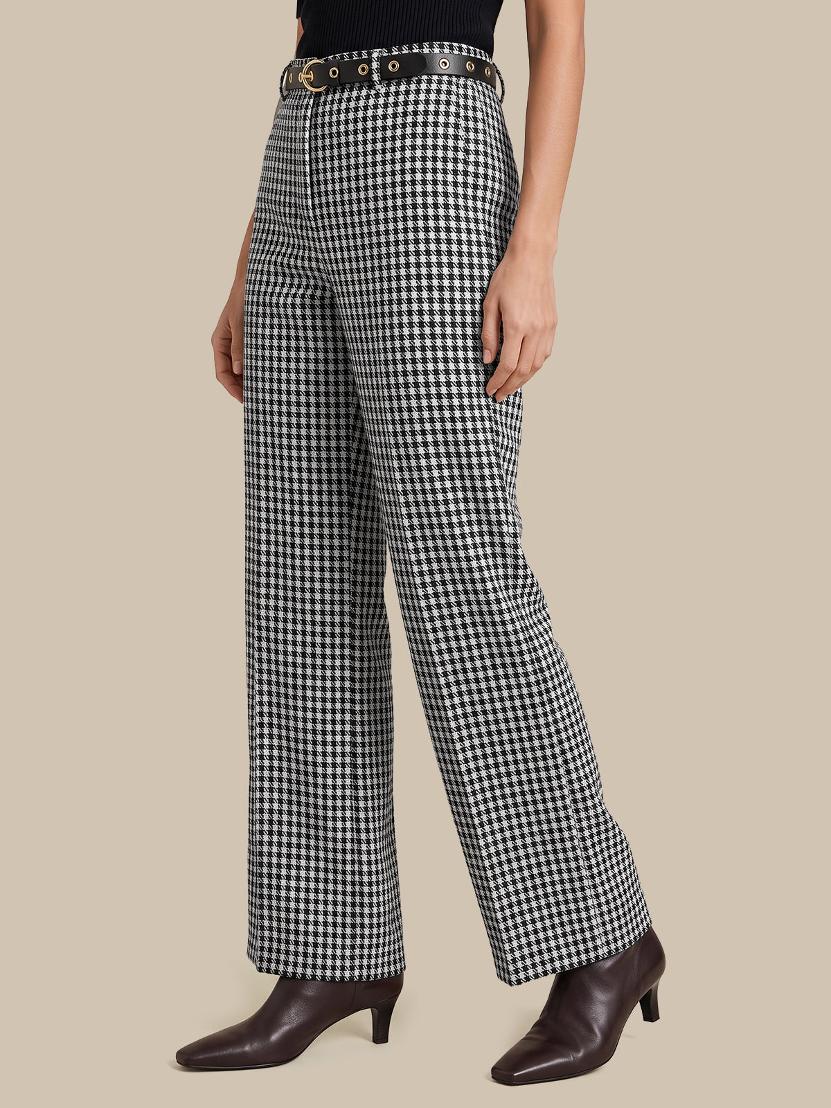 A model wearing black and white gingham wide-leg trousers with a black belt, paired with dark brown pointed-toe heeled ankle boots, against a solid beige background.