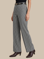 A model wearing black and white gingham wide-leg trousers with a black belt, paired with dark brown pointed-toe heeled ankle boots, against a solid beige background.
