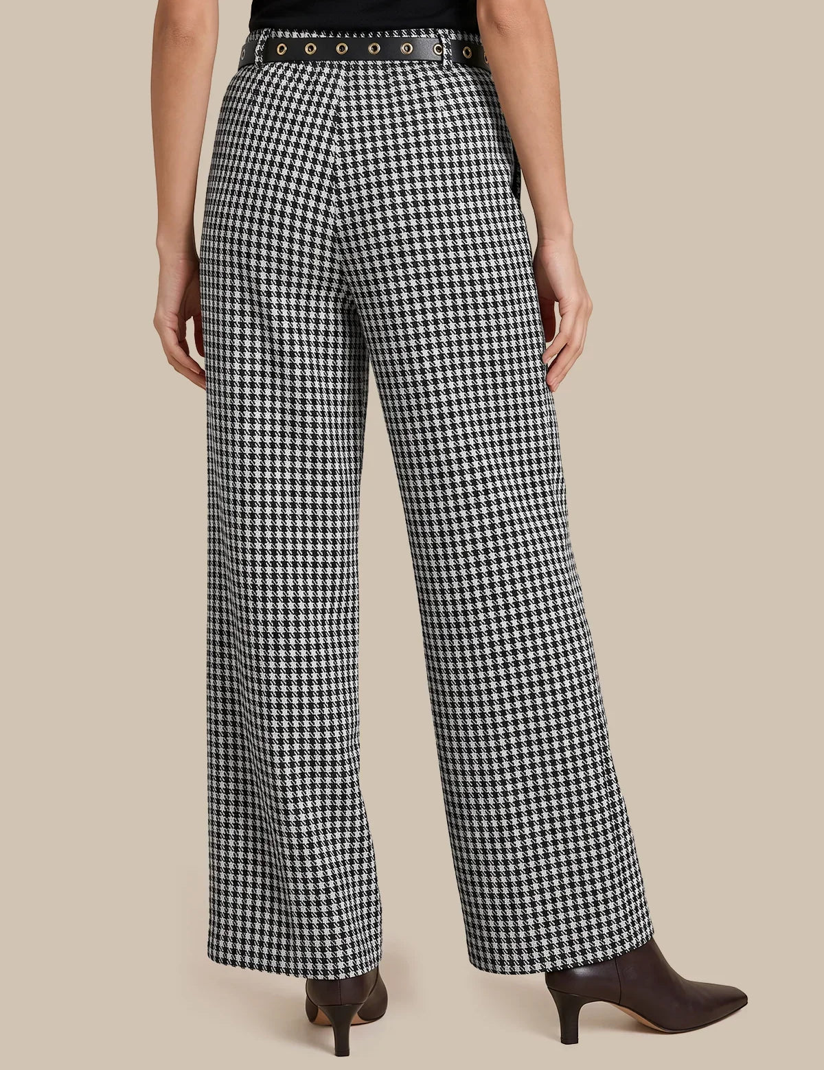 Black and white houndstooth wide-leg trousers with a studded belt, modeled from the back against a solid beige background.