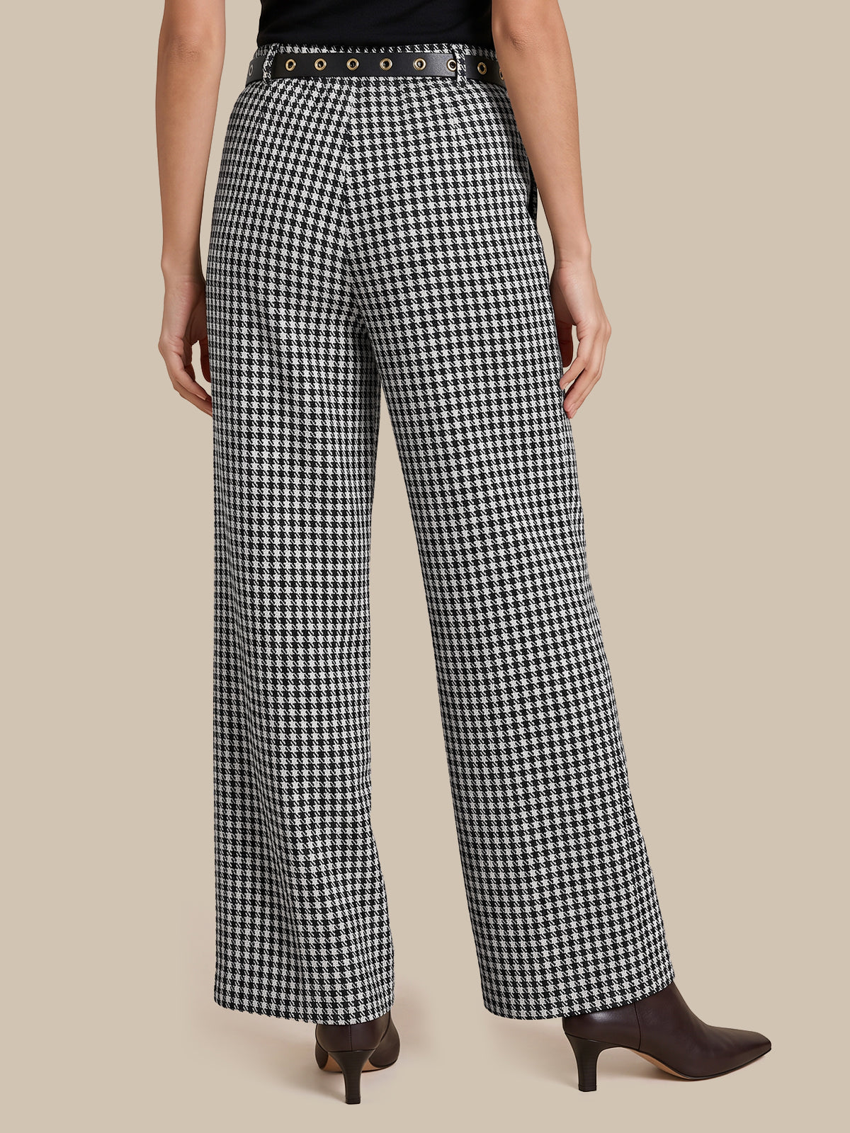 Black and white houndstooth wide-leg trousers with a studded belt, modeled from the back against a solid beige background.