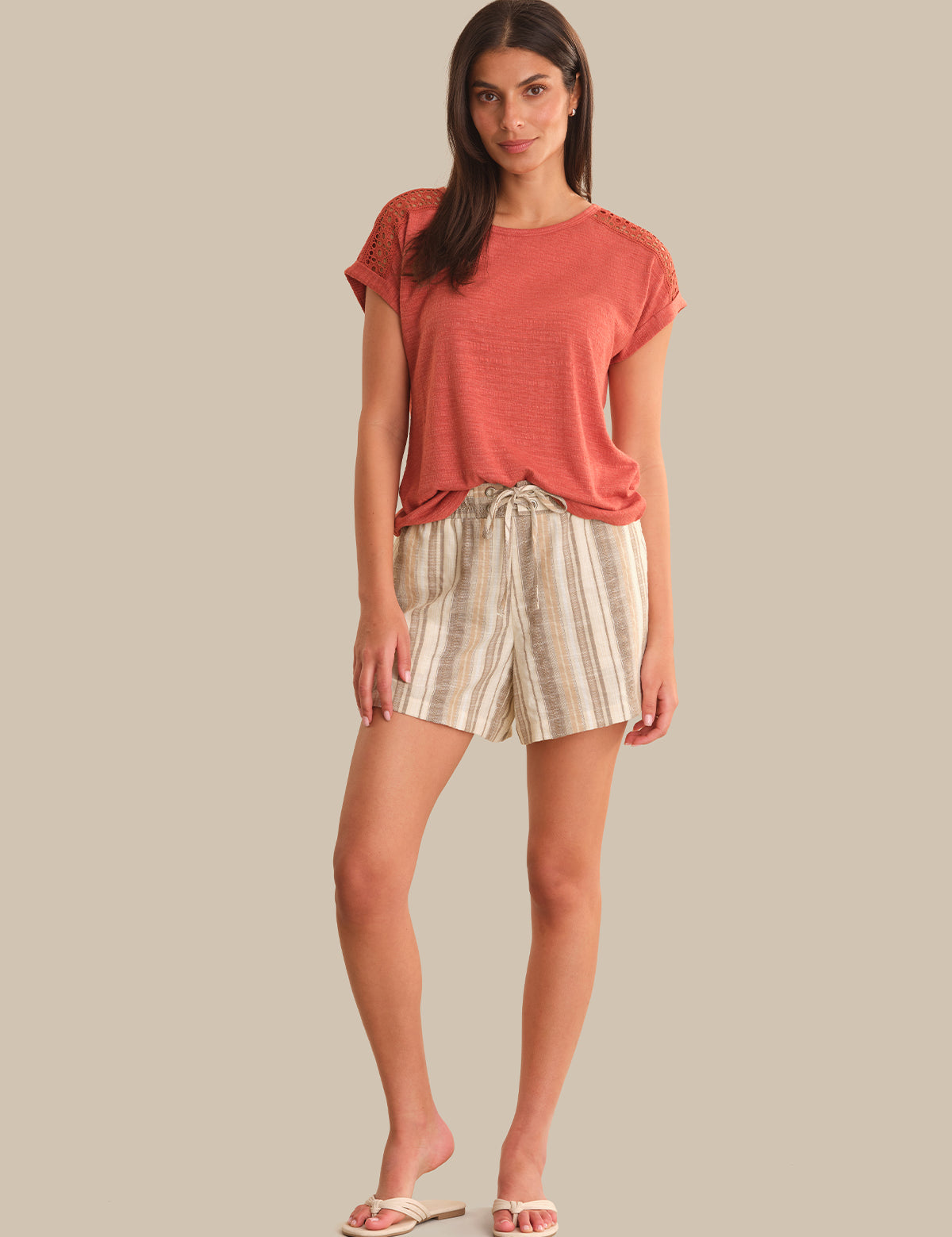 Woman wearing a coral top and plaid shorts on a beige background