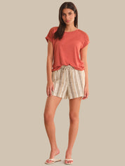 Woman wearing a coral top and plaid shorts on a beige background