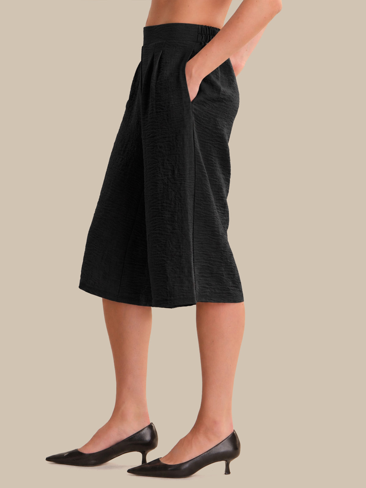 Person wearing black wide-leg pants on a beige background