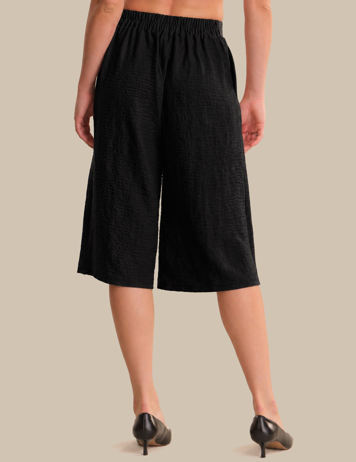 Person wearing black wide-leg pants on a beige background