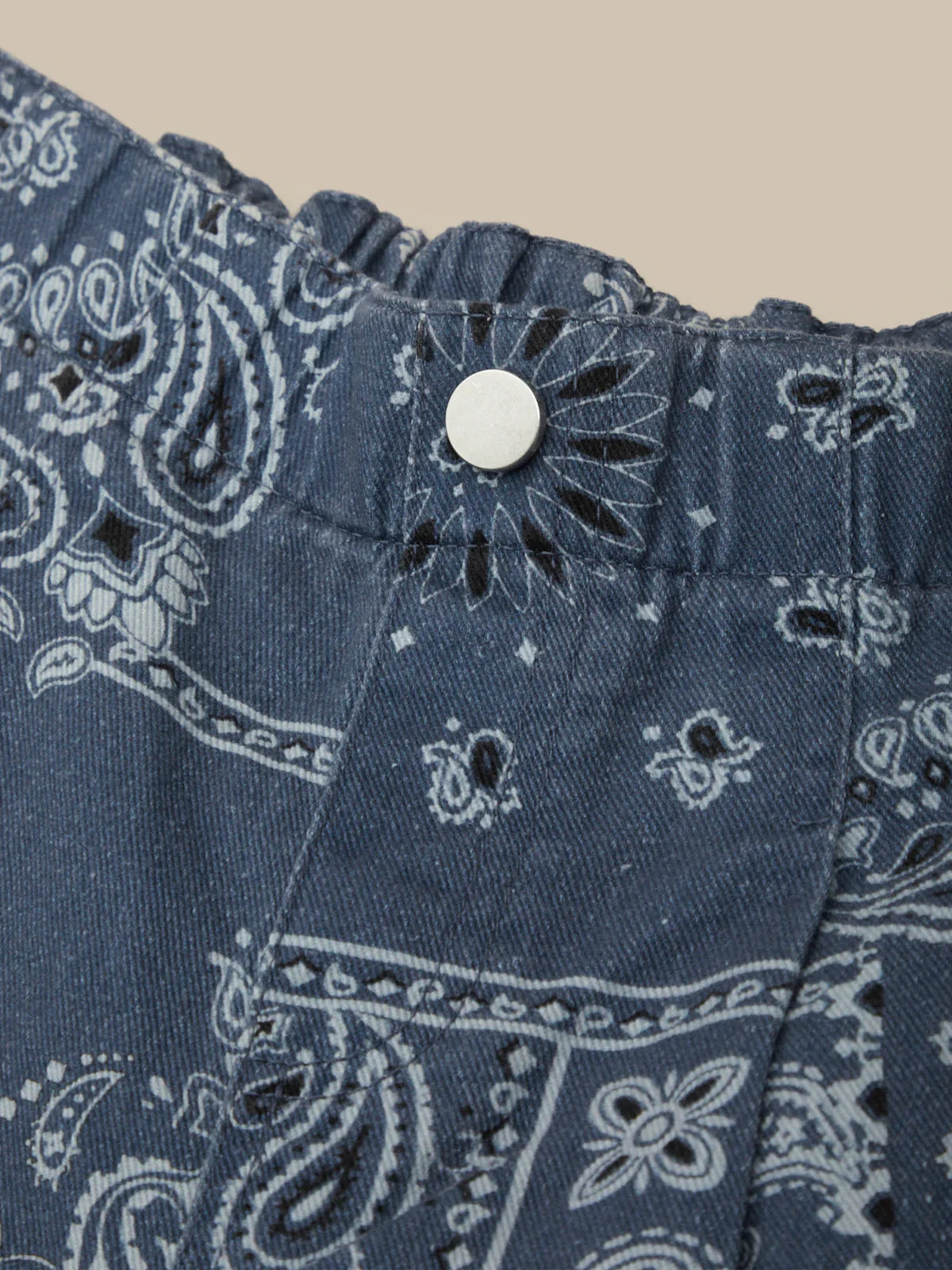 Close-up of blue bandana patterned fabric with a button on a beige background