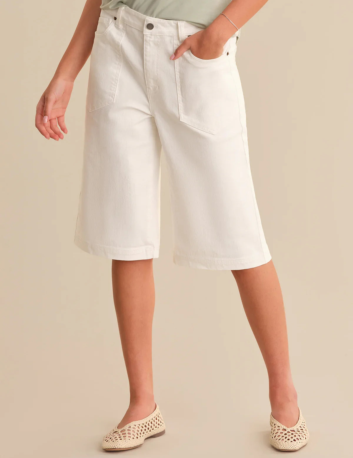 Person wearing white denim shorts on a beige background