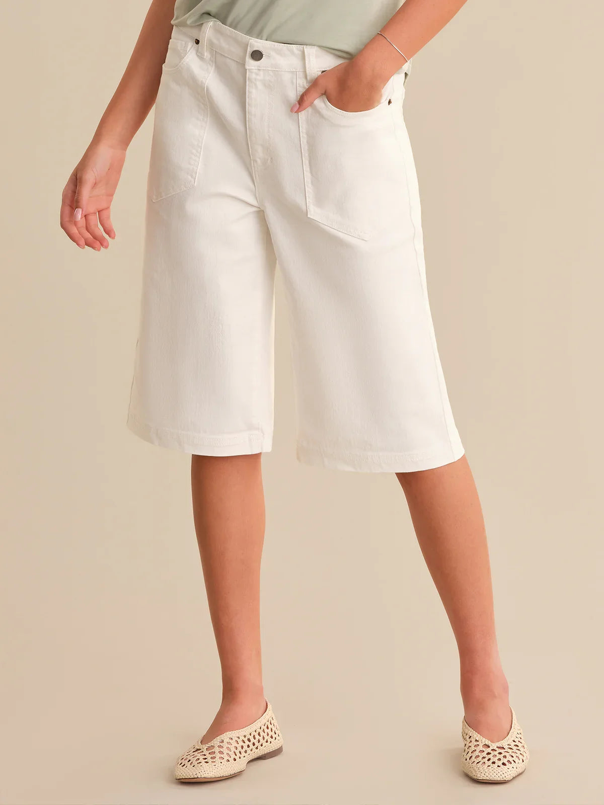 Person wearing white denim shorts on a beige background