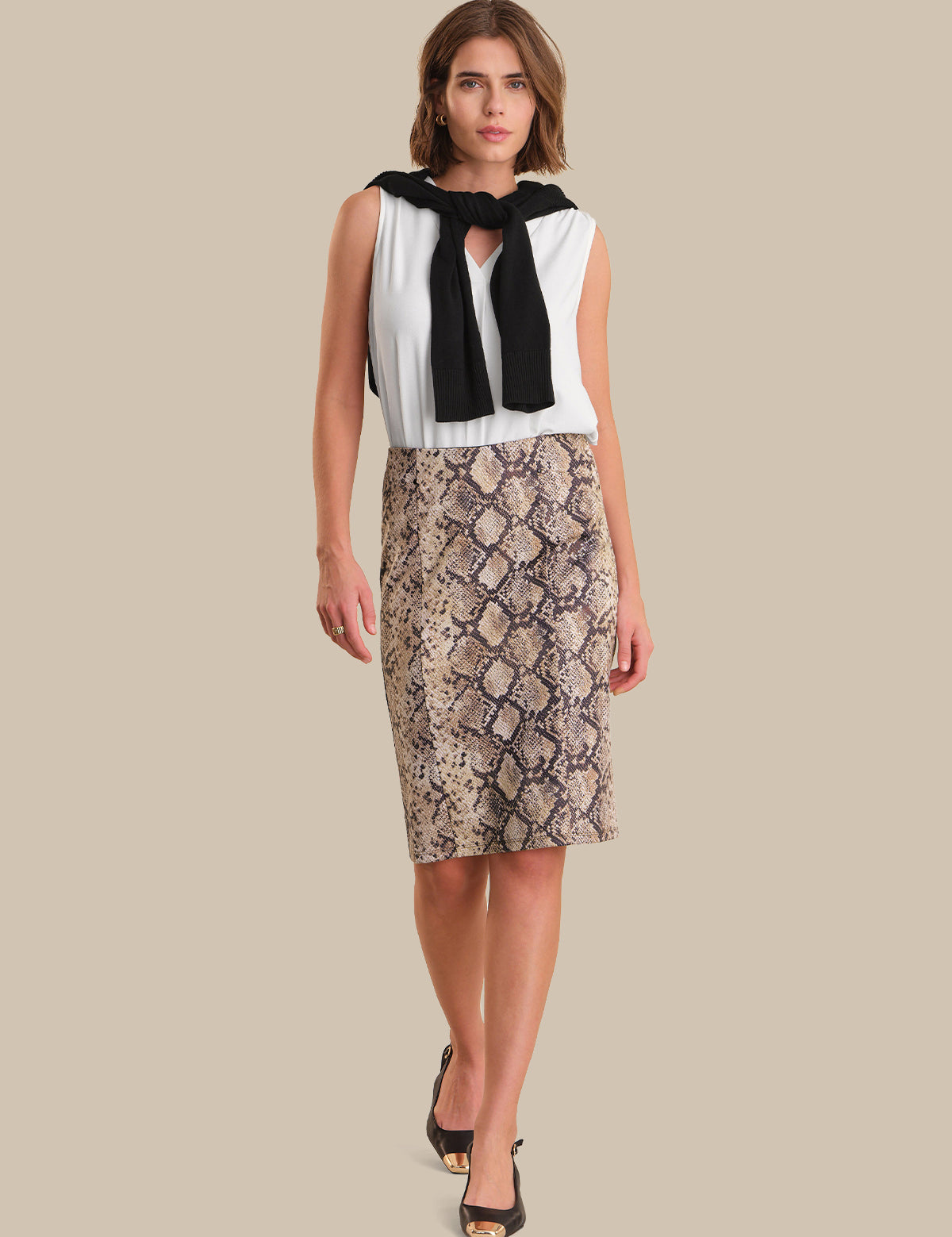 Woman wearing a white blouse with black accents and a snake print skirt on a beige background